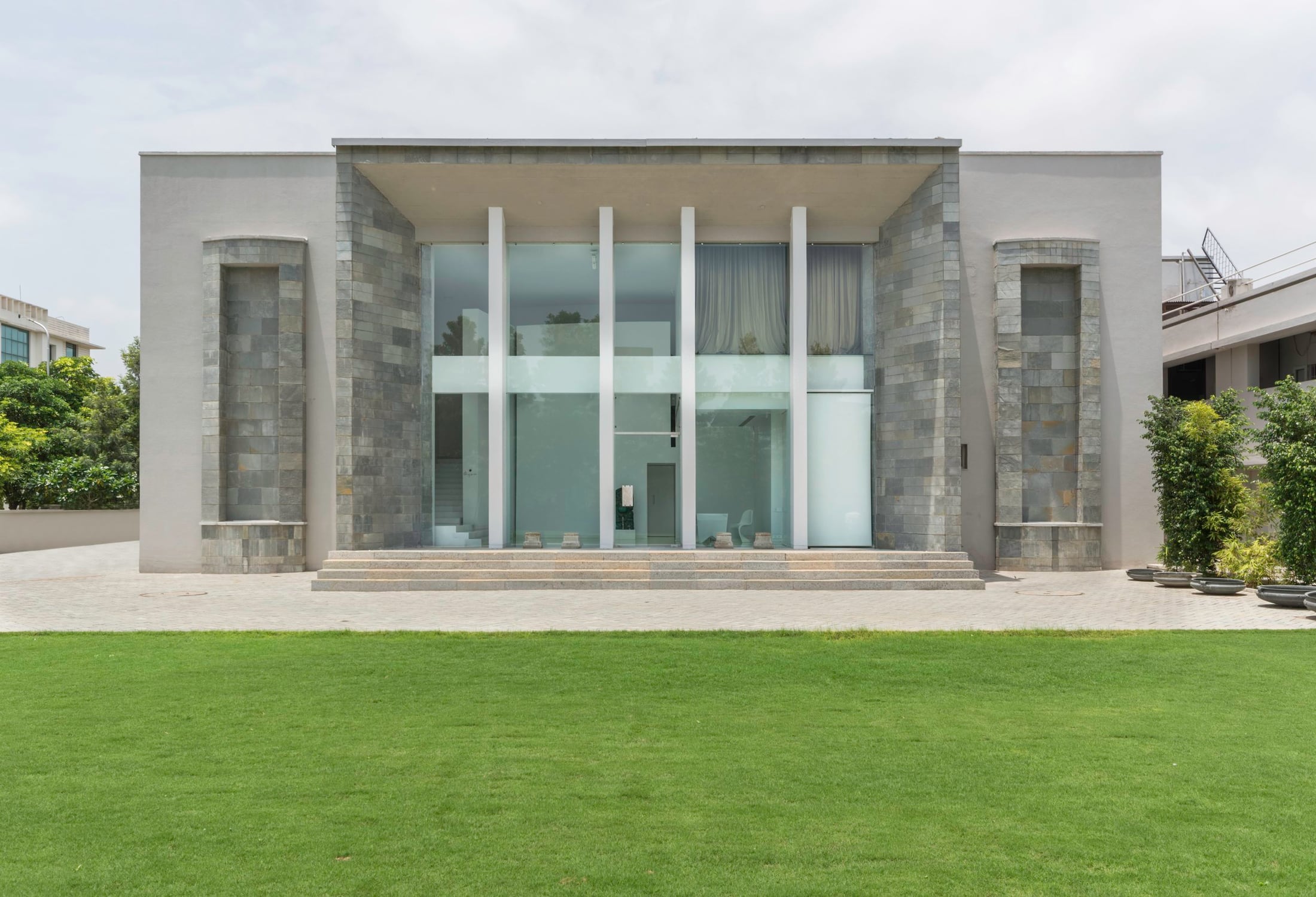 La fachada del Museo Gyan: piedra y vidrio tras un césped, con pilares altos y sobrios y unos escalones.
