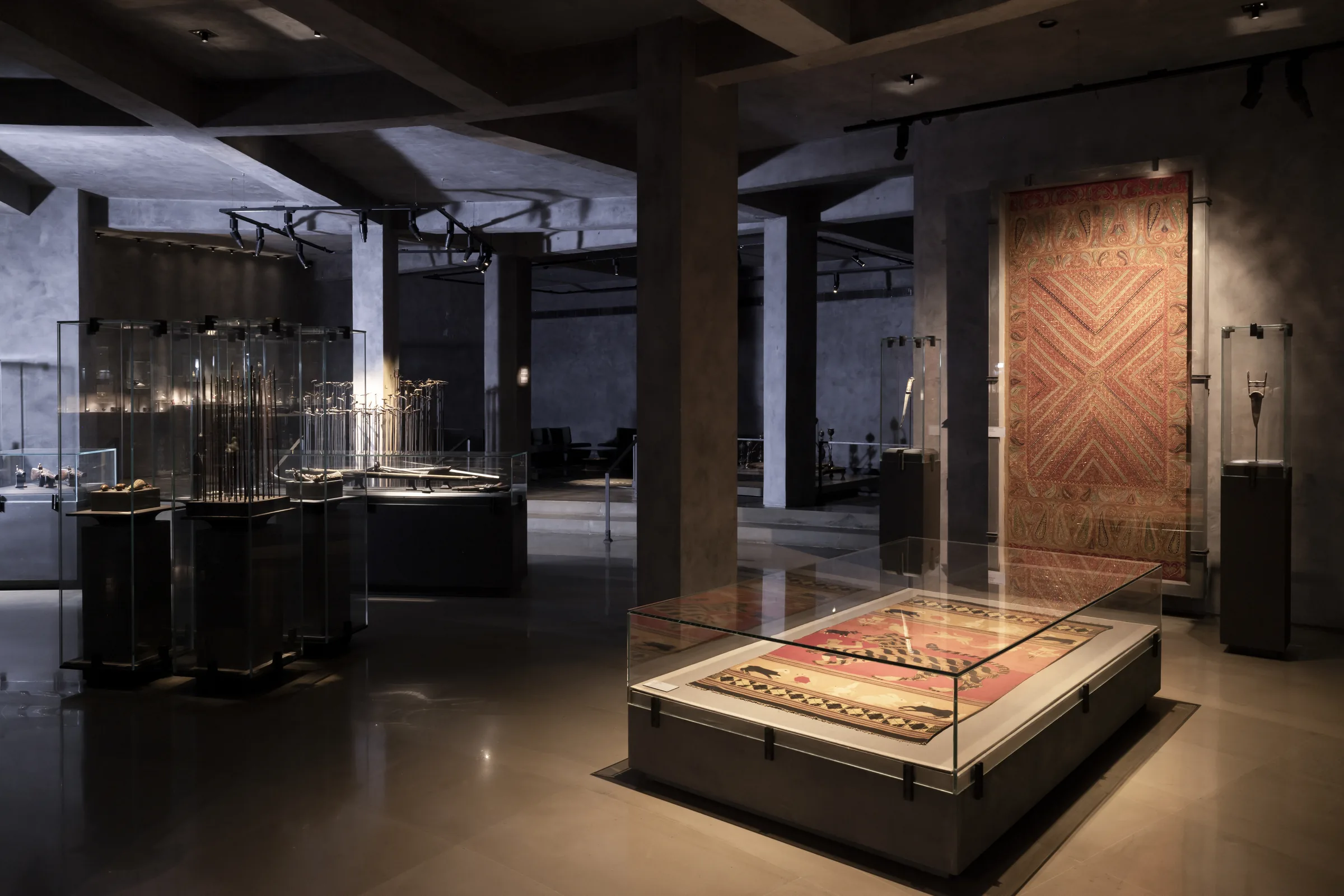 A gallery of carpets and woven panels around a central lit case.
