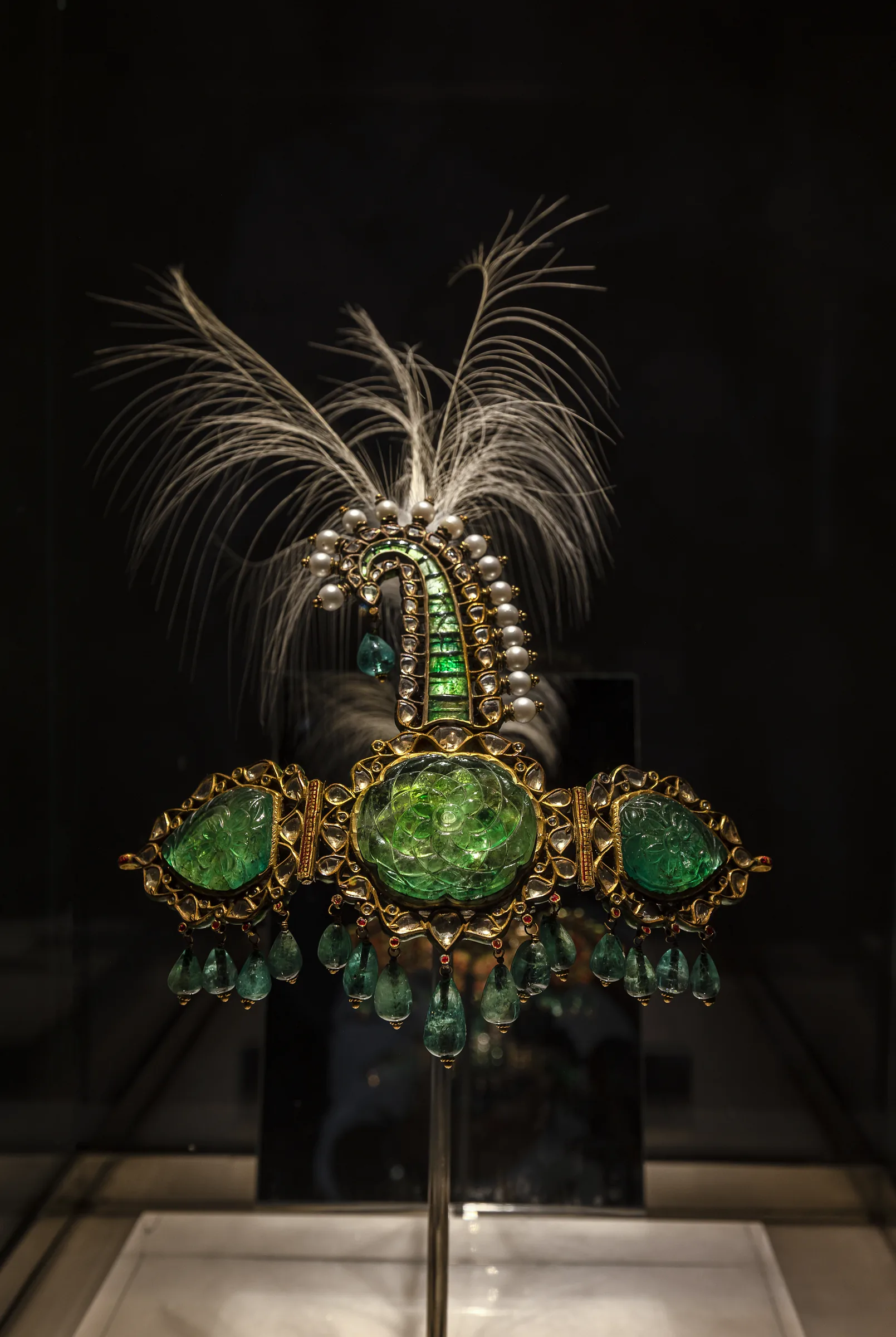 An emerald-set turban ornament with a feather plume, lit alone in its case