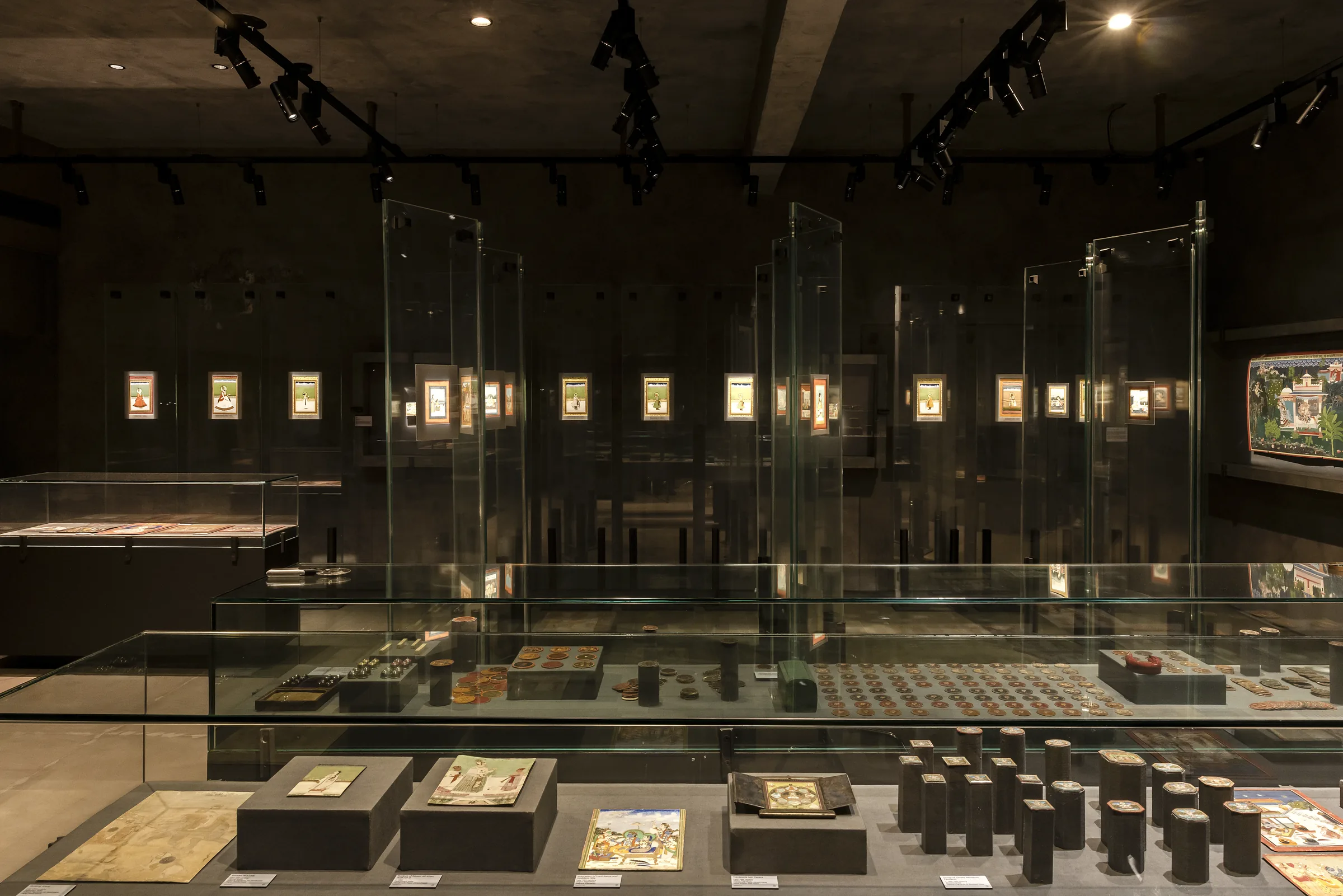 Une salle de portraits miniatures encadrés derrière des vitres, avec des vitrines de monnaies et de peintures au premier plan.