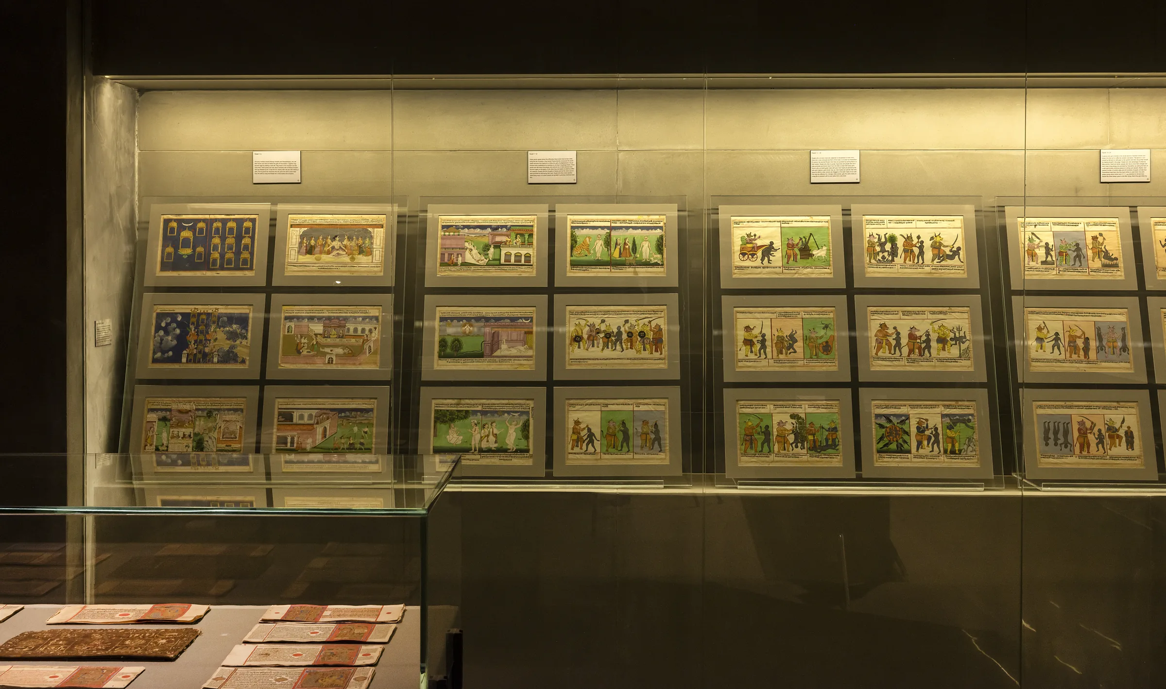 A lit wall of framed miniature paintings above a case of manuscript folios.